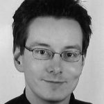 Stefan Marx Schwarz-weiß Porträt eines Mannes mit Brille und kurzen, dunklen Haaren, lächelnd in die Kamera blickend.