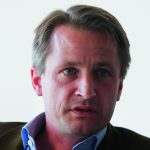 Nikolaus Blome Porträt eines Mannes mit kurzen, blonden Haaren und blauen Augen, der ernst in die Kamera schaut.