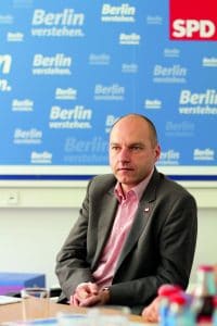 Mann in Anzug sitzt vor einer Wand mit SPD-Logos und dem Schriftzug "Berlin verstehen".