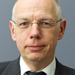 Christian Wagner Porträt eines Mannes mit Brille, kurzen grauen Haaren, in einem Anzug vor einem grauen Hintergrund.