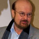 Stefan Bernhard Eck Porträt eines Mannes mit Brille, Bart und Anzugjacke, der ernst in die Kamera schaut.