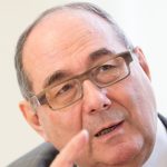 Johannes Neukirchen Nahaufnahme von Johannes Neukirchen, der während eines Interviews spricht, mit Brille und ernstem Ausdruck.