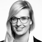 Katrin Albsteiger Porträt einer lächelnden Frau mit blonden Haaren und Brille, vor neutralem Hintergrund.