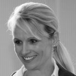 Claudia Bender Porträt einer lächelnden Frau mit blonden Haaren, die zu einem Pferdeschwanz gebunden sind, vor einem hellen Hintergrund.