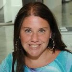 Jennifer Lawless Porträt einer lächelnden Frau mit langen, dunklen Haaren und großen Ohrringen, trägt ein buntes Oberteil.