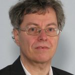 Malte Ristau Porträt eines Mannes mit Brille und grauen Haaren, in einem schwarzen Anzug vor einem hellen Hintergrund.