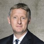 Klaus Lintemeier Porträt eines Mannes mit kurzem, blondem Haar, in einem Anzug, vor einer neutralen, grauen Wand.