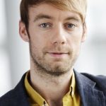 Johannes Hillje Porträt eines Mannes mit blonden Haaren, blauen Augen, in einem gelben Hemd und dunklem Blazer, neutraler Hintergrund.