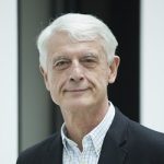 Werner Sonne Porträt eines älteren Mannes mit grauen Haaren, in einem schwarzen Blazer und karierten Hemd, vor einem neutralen Hinter...