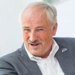 Olaf Tschimpke Olaf Tschimpke lächelt, trägt einen grauen Anzug und ein weißes Hemd, mit einem NaBu-Anstecker auf dem Revers.