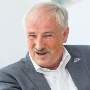 Olaf Tschimpke lächelt, trägt einen grauen Anzug und ein weißes Hemd, mit einem NaBu-Anstecker auf dem Revers.