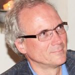Ernst-Christoph Stolper Porträt eines Mannes mit grauen Haaren und Brille, der in einem Anzug mit blauer Hemd lächelt.