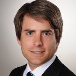 Wolfgang König Porträt eines Mannes mit braunen Haaren und blauen Augen, der einen schwarzen Anzug und eine Krawatte trägt.