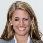 Verena Köttker Porträt einer lächelnden Frau mit blonden Haaren, in einem grauen Blazer, vor einem hellen Hintergrund.
