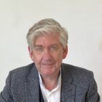 Torsten Oltmanns Foto zNT Mann mit grauen Haaren und Brille, sitzt an einem Tisch und schreibt auf ein Blatt Papier.