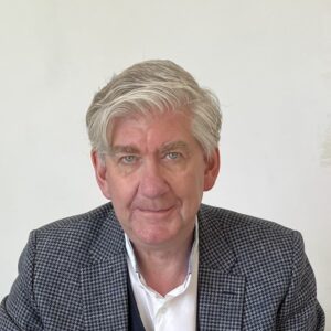 Torsten Oltmanns Foto zNT Mann mit grauen Haaren und Brille, sitzt an einem Tisch und schreibt auf ein Blatt Papier.