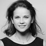 Daniela Hohmann Porträt einer lächelnden Frau mit kurzen, lockigen Haaren, in Schwarz-Weiß, vor neutralem Hintergrund.