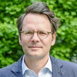 Knut Bergmann Porträt eines Mannes mit Brille und unordentlichem Haar, vor einem grünen Hintergrund.