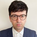 Sven Weizenegger Porträt eines Mannes mit dunklen Haaren und Brille, der einen Anzug trägt, vor einem neutralen Hintergrund.