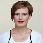 Katja Kipping (Linke) Porträt von Katja Kipping mit kurzem, rotem Haar und rotem Lippenstift, in einem weißen Oberteil vor neutralem Hintergrund.