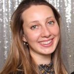 Lächelnde Frau mit langen, braunen Haaren vor einem glitzernden Hintergrund. Sie trägt ein schwarzes Oberteil.
