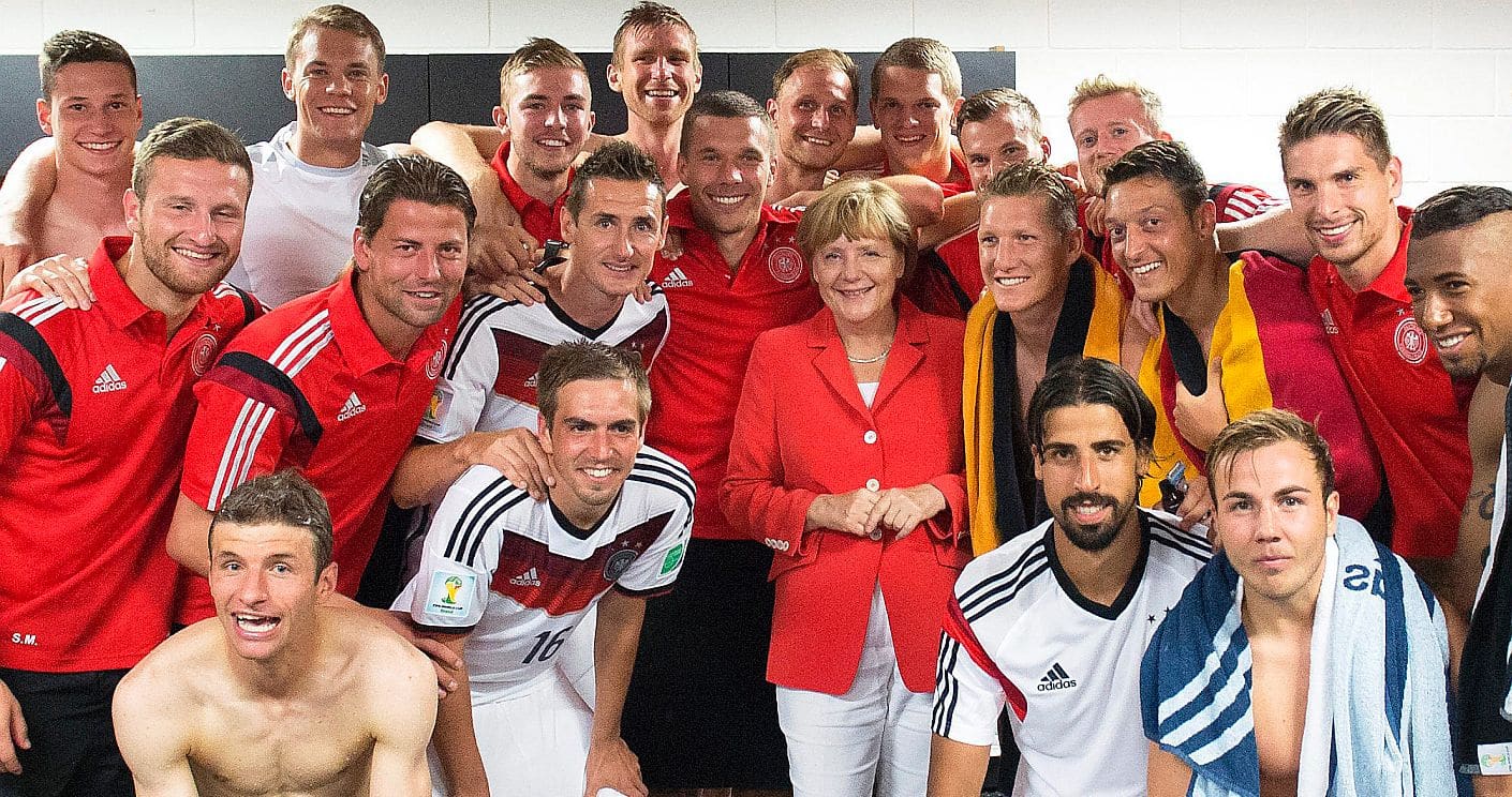 Die damalige Bundeskanzlerin Angela Merkel (CDU) besucht die deutsche Fußballnationalmannschaft nach dem Auftaktsieg gegen Portugal bei der WM 2014 in Salvador, Brasilien in der Kabine. (c) picture alliance/dpa/Guido Bergmann