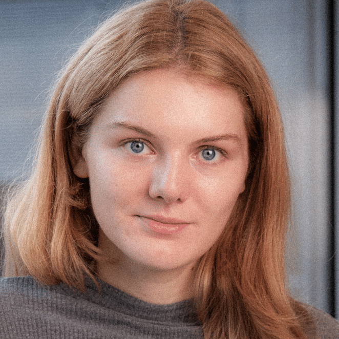 Porträt einer jungen Frau mit langen, blonden Haaren und blauen Augen, die direkt in die Kamera schaut.