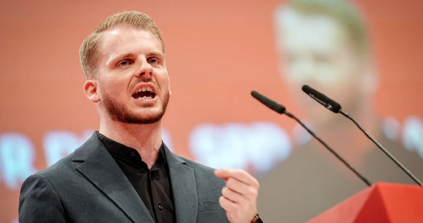 Mann spricht leidenschaftlich am Rednerpult, im Hintergrund verschwommene Projektion.