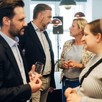 Gruppengespräch in einem modernen Raum; Personen in formeller Kleidung, einige mit Getränken in der Hand.