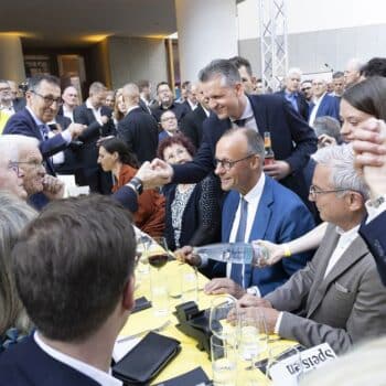 Menschen in formeller Kleidung sitzen an einem Tisch, während sie miteinander sprechen und Getränke austauschen.