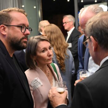 Gruppe von Menschen in formeller Kleidung, die in einem Gespräch vertieft sind, mit Getränken in der Hand.