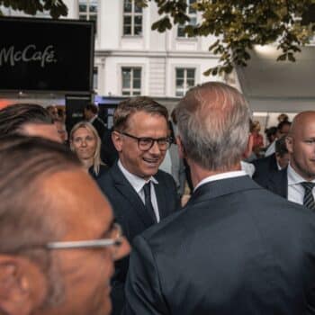 Menschen in Anzügen unterhalten sich auf einer Veranstaltung, im Hintergrund ein McCafé-Stand und Bäume.