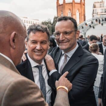 Vier Männer in Anzügen stehen zusammen, lächeln und unterhalten sich auf einer Veranstaltung im Freien.