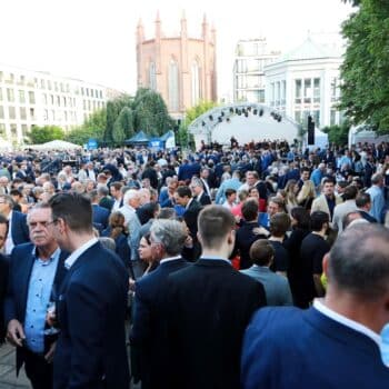 Große Menschenmenge bei einer Veranstaltung im Freien, mit einem Bühnenaufbau im Hintergrund und historischen Gebäuden.