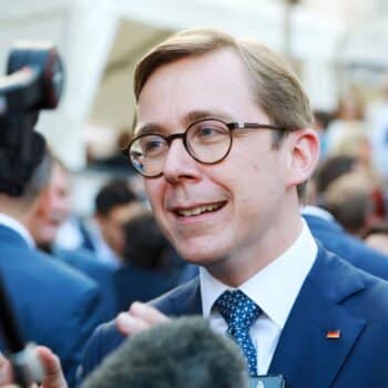 Mann mit Brille und Anzug spricht lächelnd in einer Menschenmenge, Mikrofon in der Nähe.