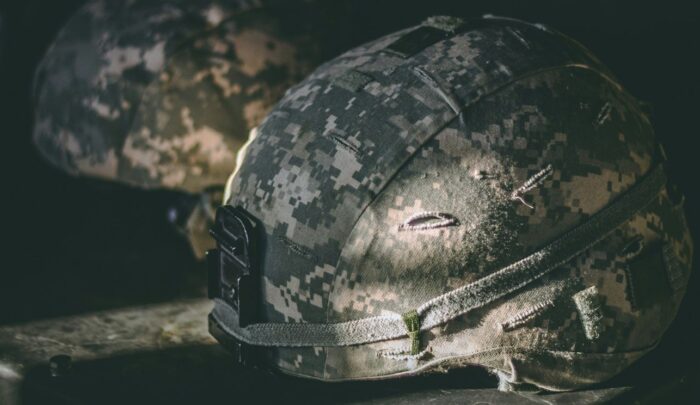 Zwei militärische Helme mit Tarnmuster liegen auf einer Oberfläche, beleuchtet von sanftem Licht.