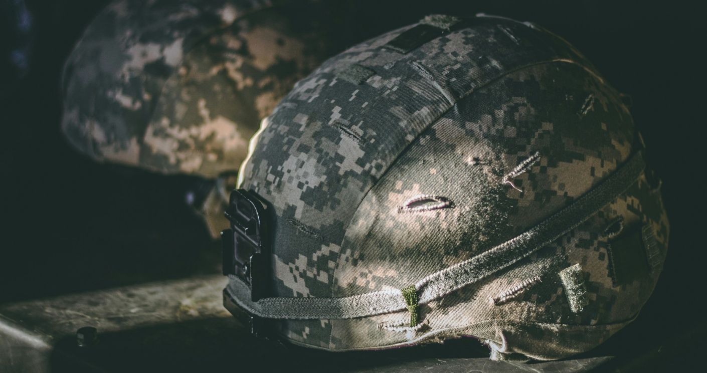 Zwei militärische Helme mit Tarnmuster liegen auf einer Oberfläche, beleuchtet von sanftem Licht.