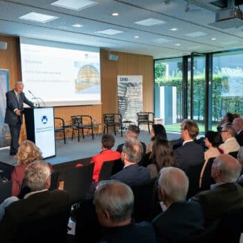 Otmar Issing spricht vor Publikum bei Preisverleihung zur Sozialen Marktwirtschaft, mit moderner Architektur im Hintergrund.
