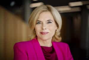 Porträt einer Frau mit blonden Haaren, die einen pinken Blazer trägt und freundlich in die Kamera lächelt.