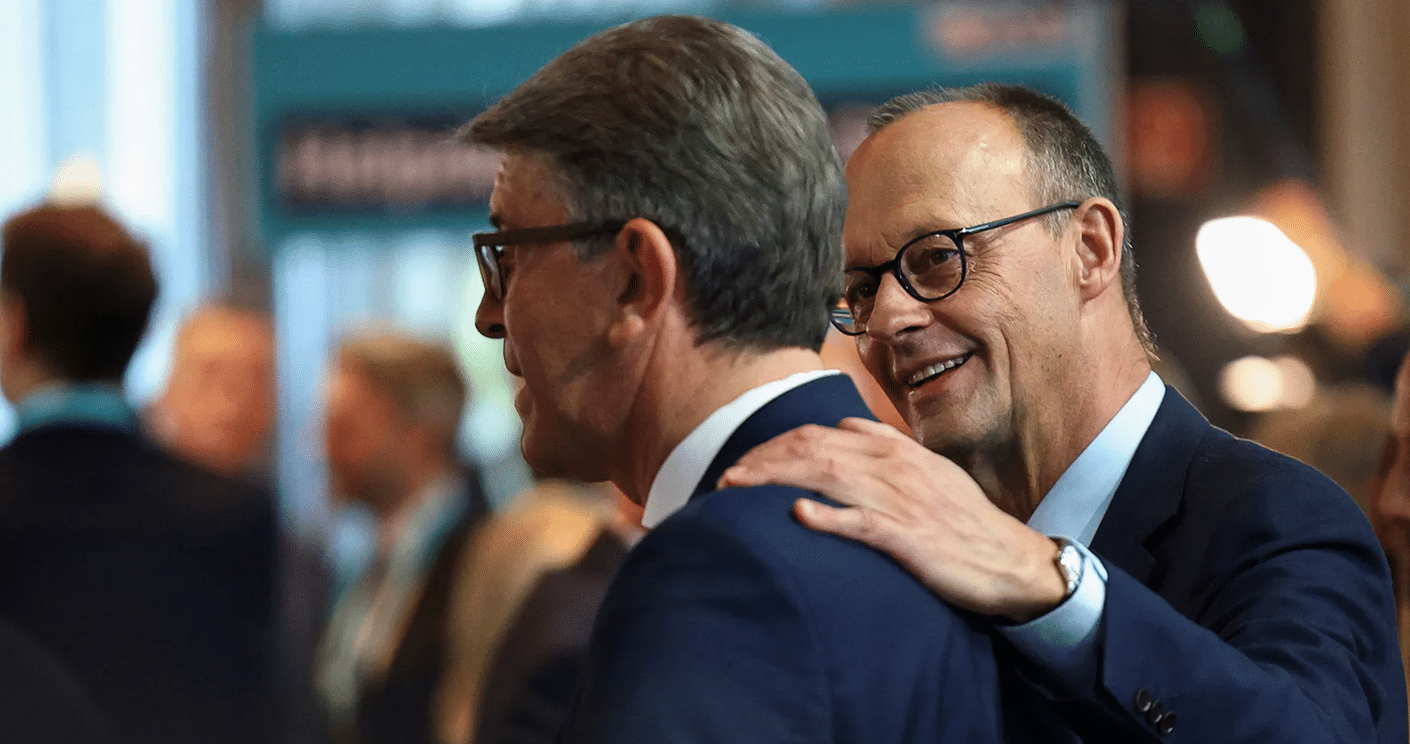 Zwei Männer in Anzügen stehen in einer geschäftlichen Umgebung, einer lächelt und legt eine Hand auf die Schulter des ...