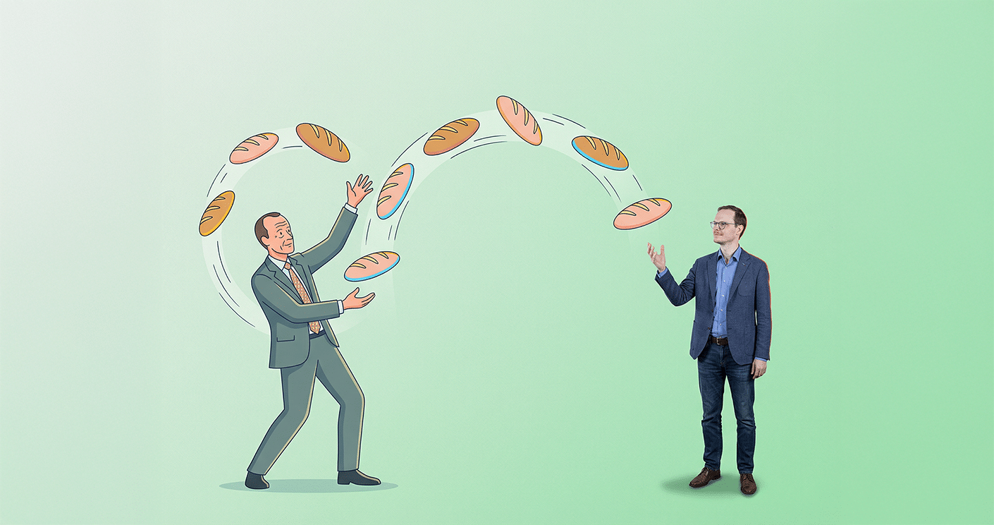 Mann im Anzug jongliert mit Broten, während ein weiterer Mann daneben steht und zuschaut, vor grünem Hintergrund.