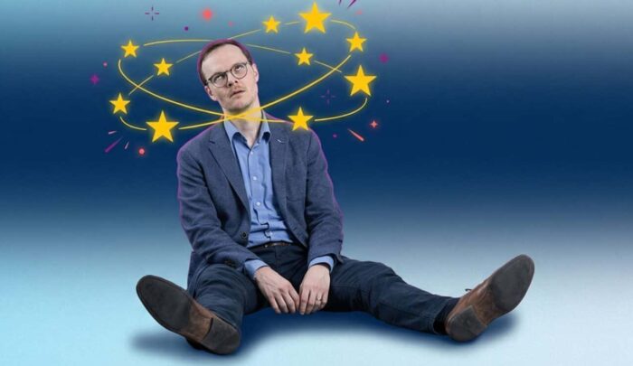 Mann sitzt mit ausgestreckten Beinen auf dem Boden, umgeben von bunten Sternen auf einem blauen Hintergrund.