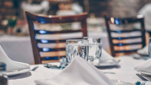 Tischgedeck in einem Restaurant mit weißen Tischdecken, Gläsern, Besteck und gefalteten Servietten.