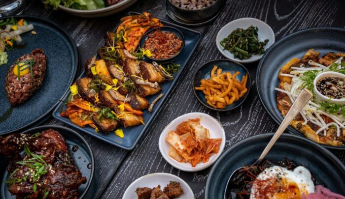 Vielfalt an asiatischen Gerichten auf dunklen Tellern, darunter Fleisch, Gemüse, Reis und Beilagen.