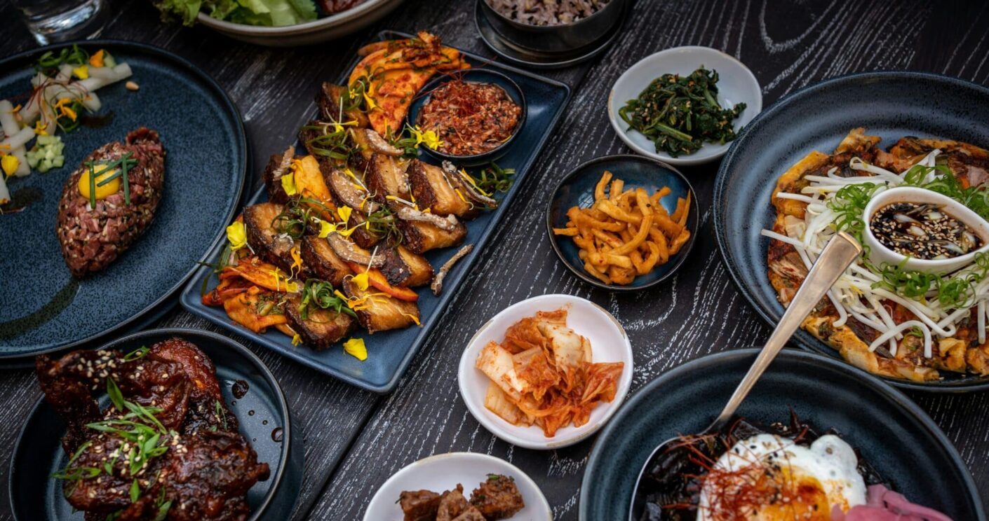 Vielfalt an asiatischen Gerichten auf dunklen Tellern, darunter Fleisch, Gemüse, Reis und Beilagen.