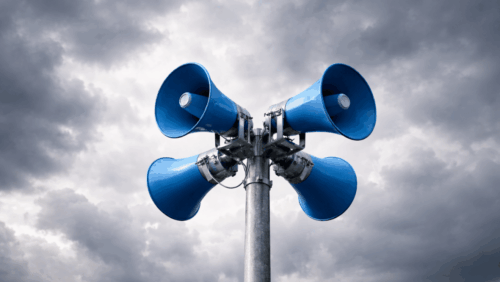 Bild: KI-generiert mit ChatGPT Image 1.5 Vier blaue Lautsprecher auf einem Metallmast vor einem bewölkten Himmel.