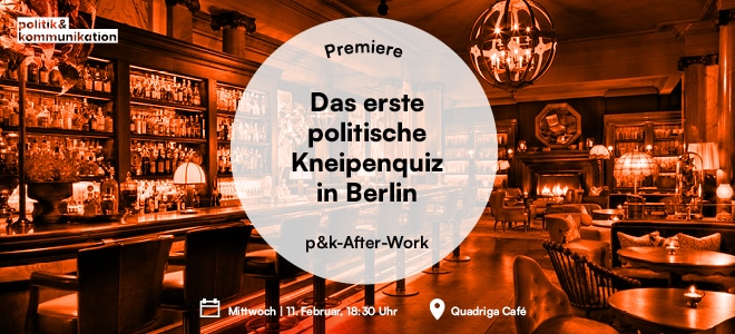 Ein elegantes Café mit Holzregalen, warmem Licht und einer Ankündigung für ein politisches Kneipenquiz in Berlin.