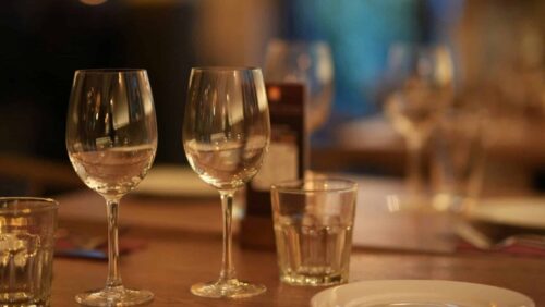 Foto: Small giant/unsplash Zwei Weingläser und ein Wasserglas auf einem gedeckten Tisch, sanfte Beleuchtung im Hintergrund.