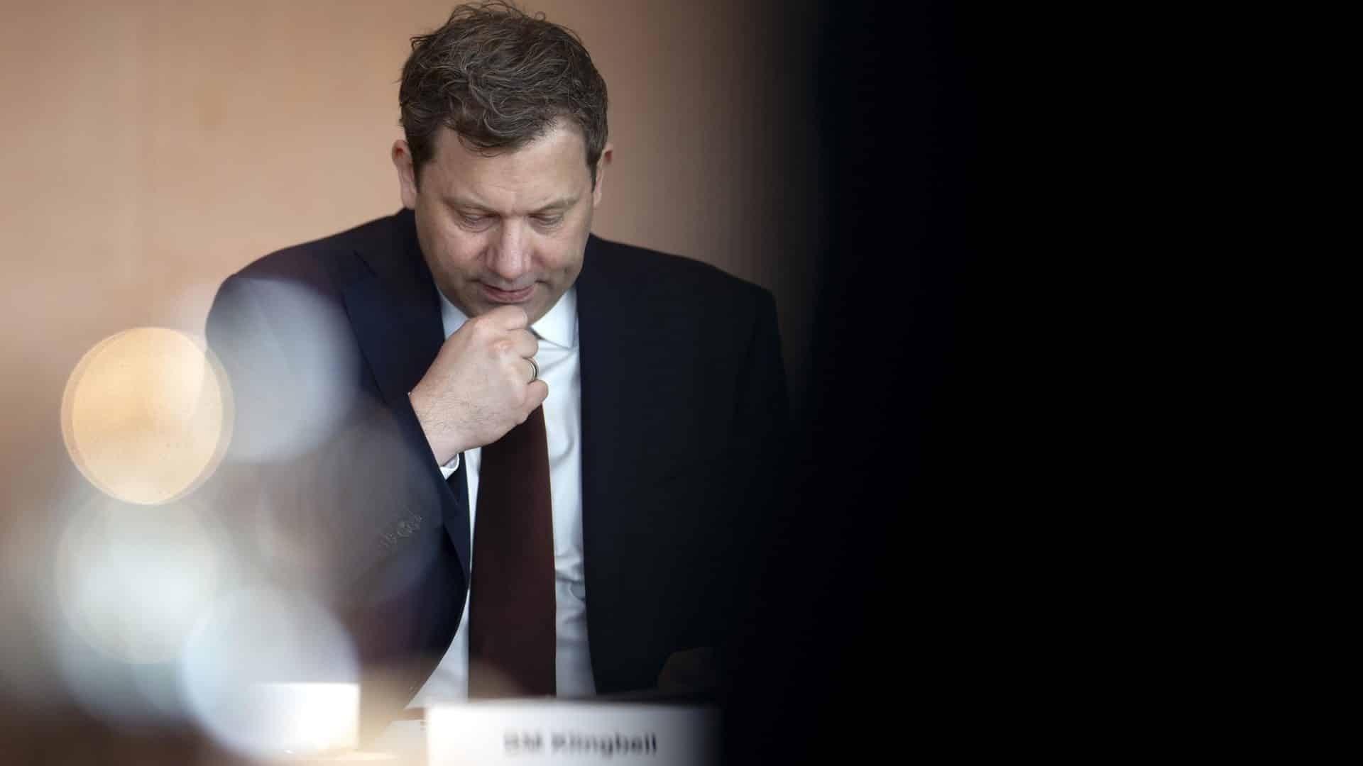 Nachdenklicher Mann in Anzug, der auf sein Handy schaut, mit unscharfem Hintergrund und Lichtreflexen.