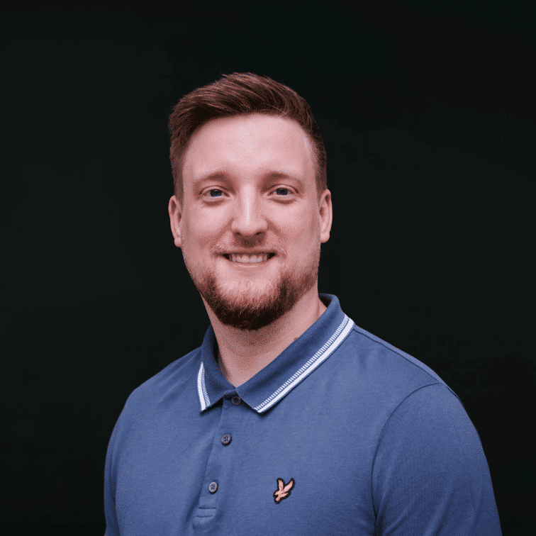 Porträt eines lächelnden Mannes mit kurzem Bart, in einem blauen Poloshirt vor einem dunklen Hintergrund.